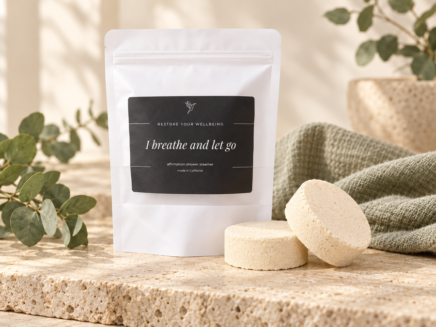 Restore Your Wellbeing affirmation shower-steamer pouch with two round pucks on warm cream stone